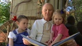 Grandparent reaching a storybook to two young granddaughters